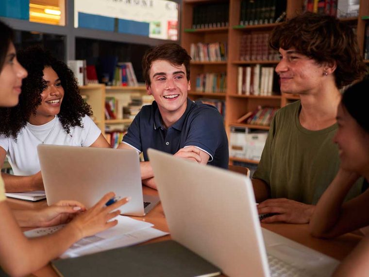 Students laughing together around laptops in a university library