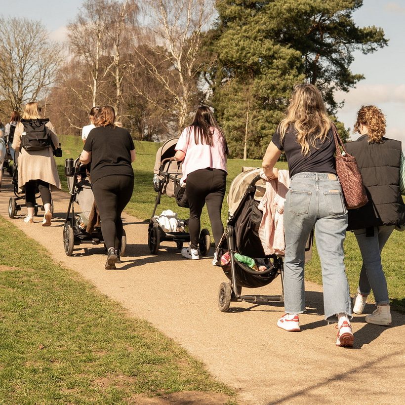 A group of parents pushing prams along a park path