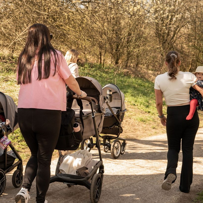 Parents walking together along a woodland path with prams
